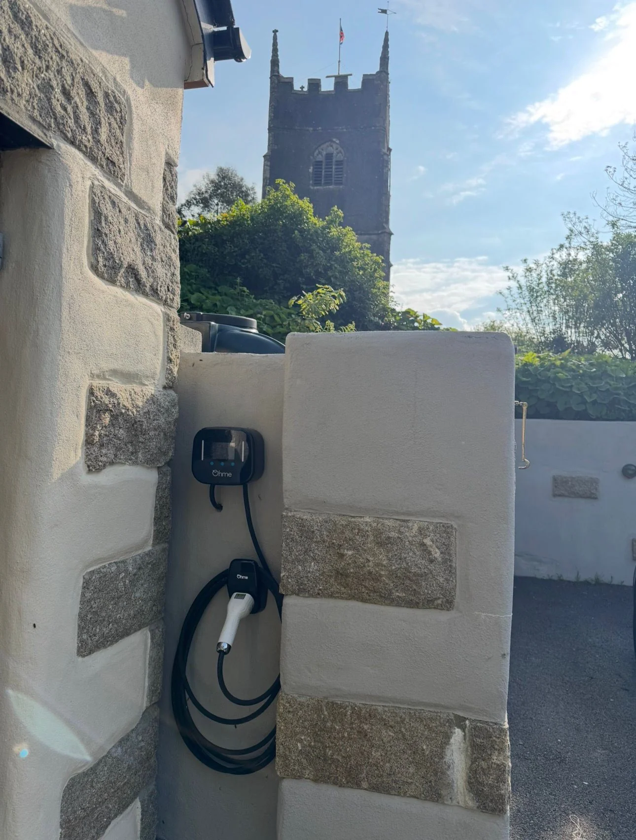 Ohme wall-mounted EV charger with a village church behind