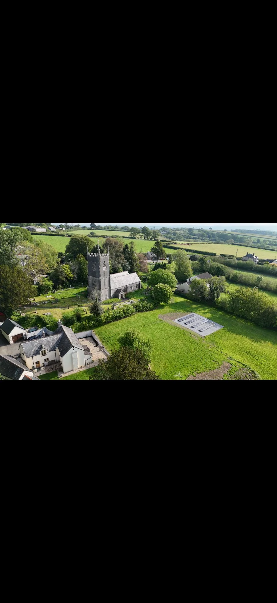 Aerial view of a village church with a nearby ground-mounted solar array